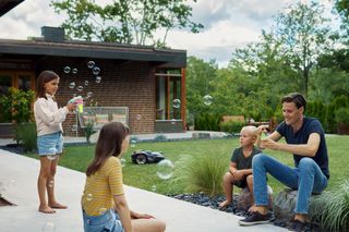 En familj som njuter av trädgården med en robotgräsklippare i bakgrunden.