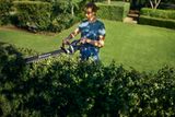 En person som trimmer en hekk med en Husqvarna-hekksaks i en hage.
