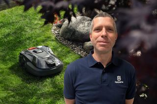 Eine Person, die in einem Garten mit einem Husqvarna Mähroboter auf dem Gras steht.