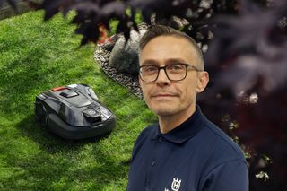 Ein Mähroboter, der in einem Garten in der Nähe von dekorativen Steinen arbeitet, wobei eine Person zu sehen ist, die ein Husqvarna T-Shirt trägt.