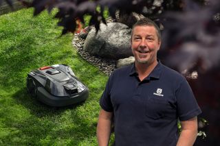 Eine Person, die in einem Garten mit einem Husqvarna Mähroboter auf dem Gras steht.