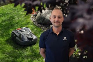 Eine Person, die in einem Garten mit einem Husqvarna Mähroboter auf dem Gras steht.