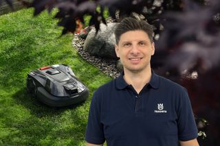 Eine Person, die in einem Garten mit einem Husqvarna Mähroboter auf dem Gras steht.