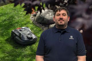 Ein Mähroboter, der auf einer Rasenfläche in der Nähe von Felsen arbeitet, mit einer Person, die im Vordergrund steht und ein Husqvarna T-Shirt trägt.