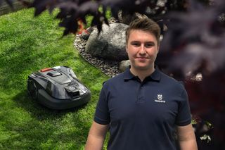 Eine Person, die in einem Garten mit einem Husqvarna Mähroboter auf dem Gras steht.