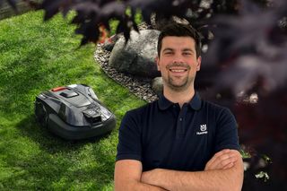 Ein Mähroboter, der auf einem Rasen in der Nähe von Felsen arbeitet, während eine Person in einem Husqvarna T-Shirt daneben steht.