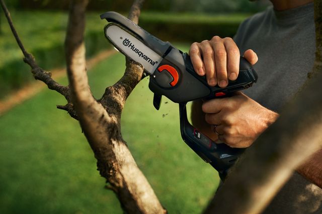 Une personne utilise une scie à élaguer Husqvarna pour tailler des branches dans un jardin.