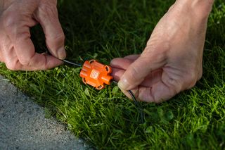 Mains ajustant un outil de jardin sur de l’herbe près d’un bord de béton.