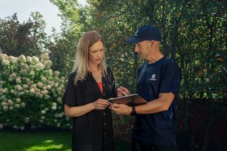 Deux personnes discutent dans un jardin, une tablette à la main.