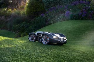 Robotic lawn mower operating on a grassy slope in a garden.