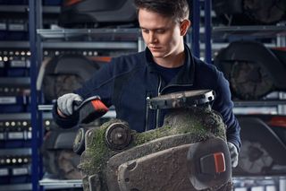Eine Person, die die Unterseite eines Husqvarna Mähroboters in einer Werkstatt inspiziert.