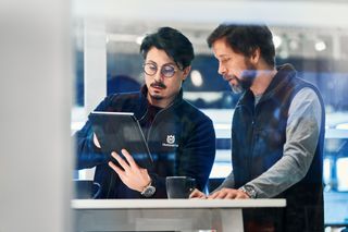 Two people discussing over a tablet in a modern office setting, with Husqvarna branding visible.