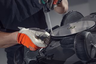 Uma pessoa usando luvas usando uma chave de fenda para ajustar um componente em uma máquina.