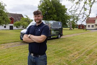 Person på en gräsmatta bredvid en Husqvarna-servicebil med marknadsföring för hembesök av robotgräsklippare.